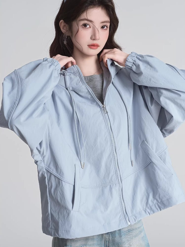 Woman adjusting the hood of her light blue jacket, highlighting the drawstring and zipper.