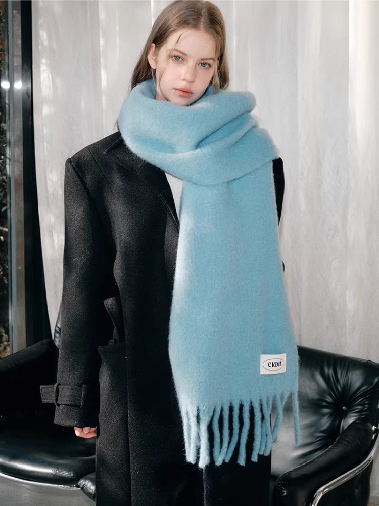 Woman in a black coat with a light blue mohair blend scarf featuring fringe and a logo tag.