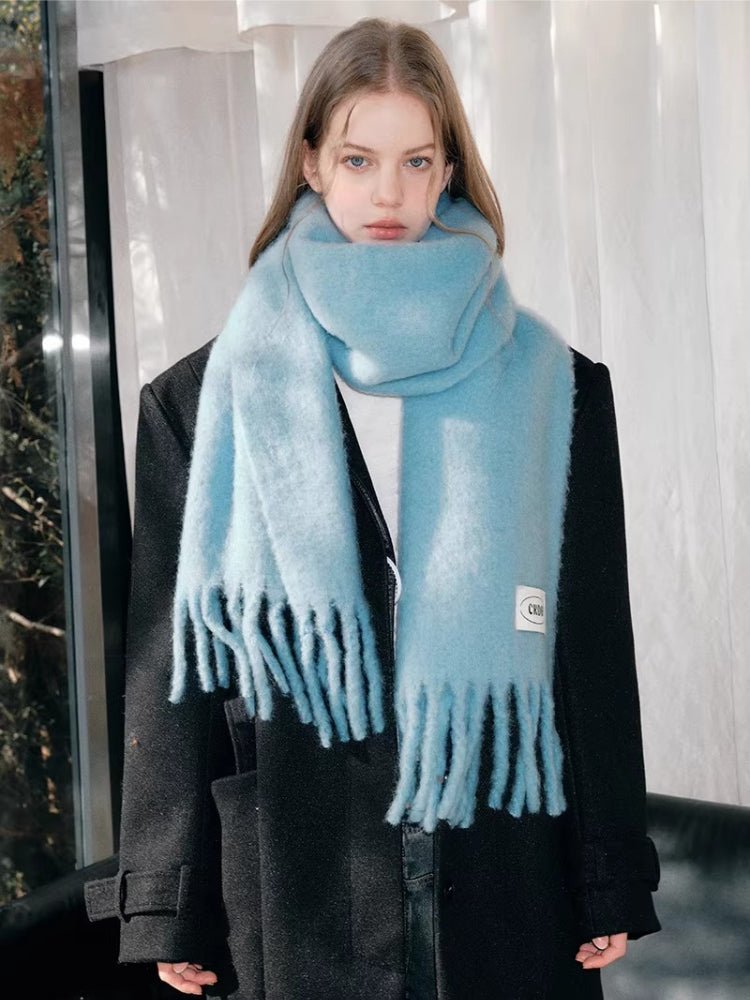 Model showcasing a light blue mohair blend scarf with fringe, styled with a black coat.
