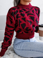 Woman sitting and holding a coffee cup while wearing a red and black leopard print knit sweater.