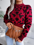Woman holding a brown fringed clutch while wearing a red and black leopard print sweater.