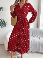 Woman in a red polka dot wrap dress with a pleated skirt and self-tie belt