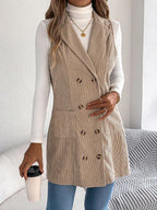 Woman wearing a longline corduroy vest in beige with a white turtleneck and blue jeans, holding a coffee cup.