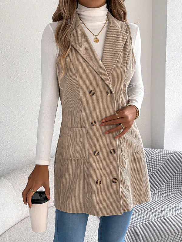 Woman wearing a longline corduroy vest in beige with a white turtleneck and blue jeans, holding a coffee cup.