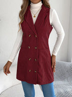 Full body shot of a woman in a burgundy corduroy vest, styled with a white turtleneck and blue jeans.