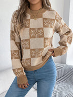 Woman wearing a tan and cream checkered knit sweater with snowflake print and crew neckline