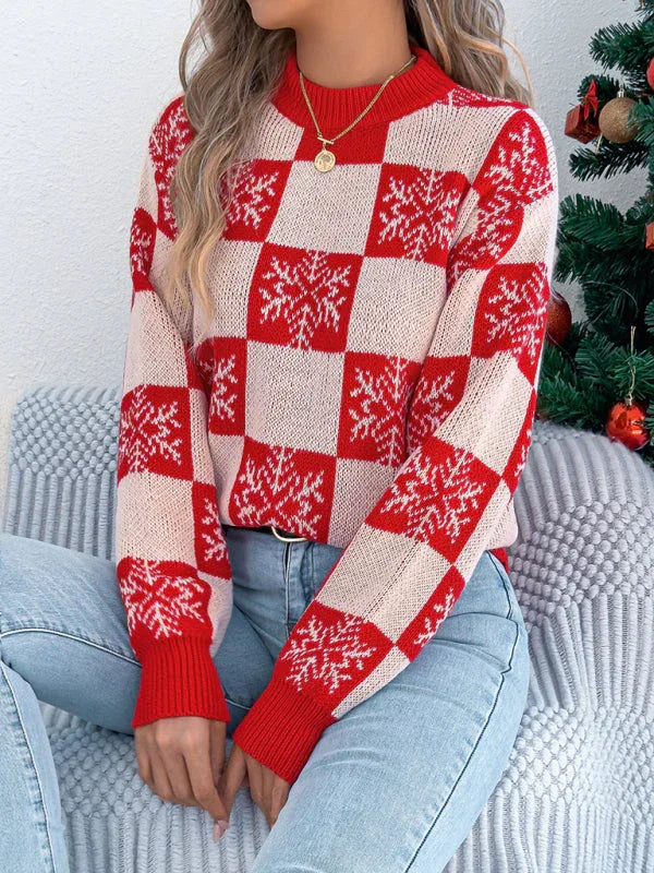 Woman sitting down wearing a red and white checkered knit sweater with snowflake print and blue jeans
