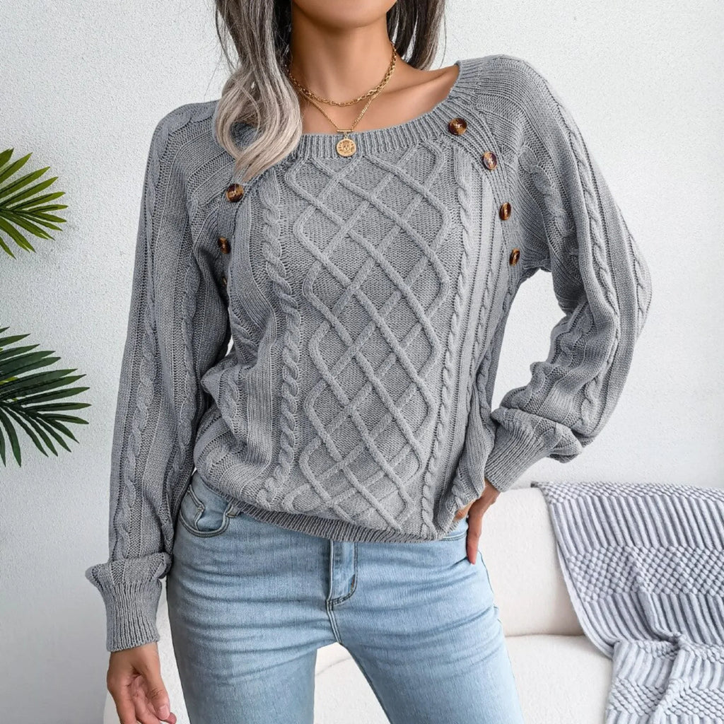 Woman wearing a grey cable knit sweater with decorative buttons and light wash denim jeans