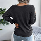 Back view of a woman wearing a dark grey cable knit sweater with cable knit sleeves and a scoop neckline.