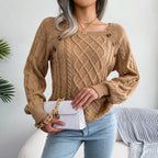 Woman wearing a tan cable knit sweater with decorative buttons on the neckline, holding a white handbag.