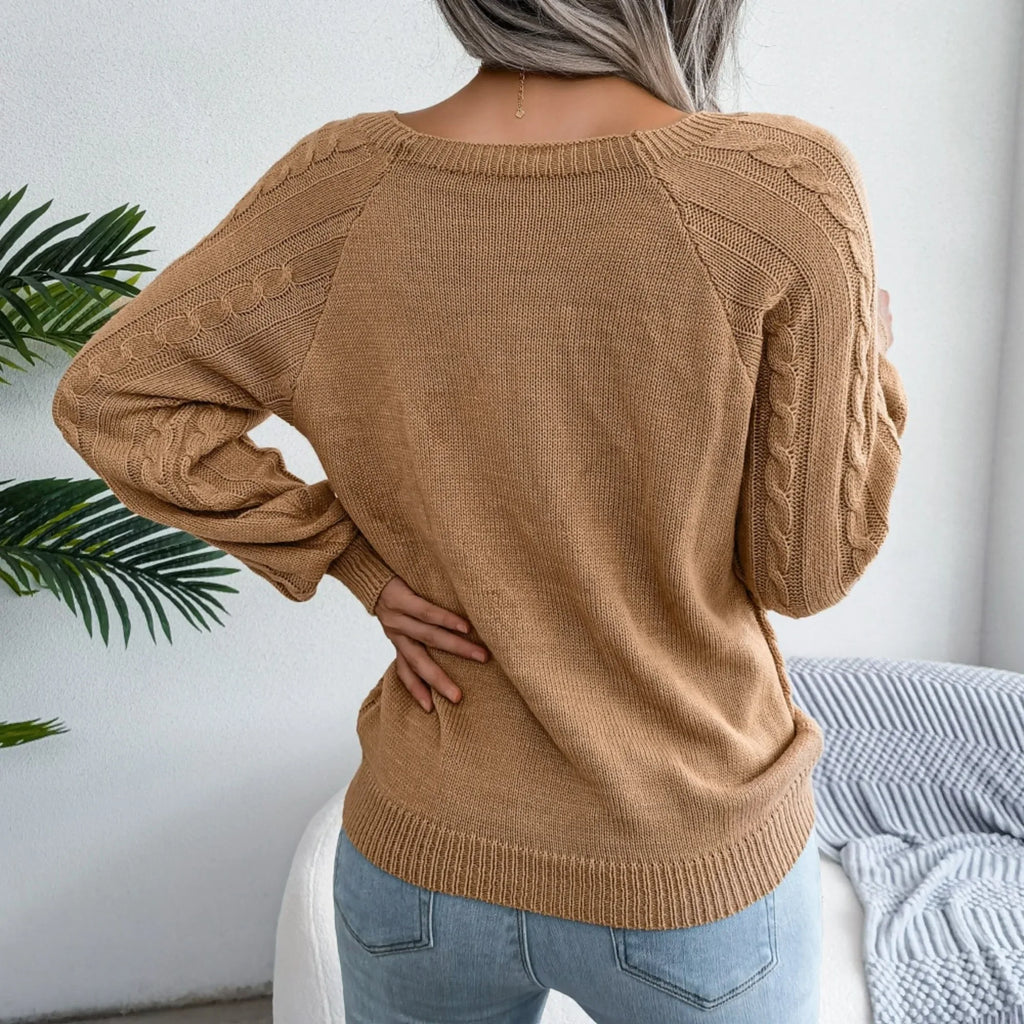 Back view of a woman wearing a tan cable knit sweater with a square neckline and decorative buttons.
