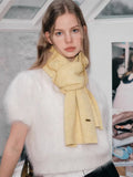 Close-up of a pale yellow knit scarf with a textured pattern and a gold-tone logo tag.