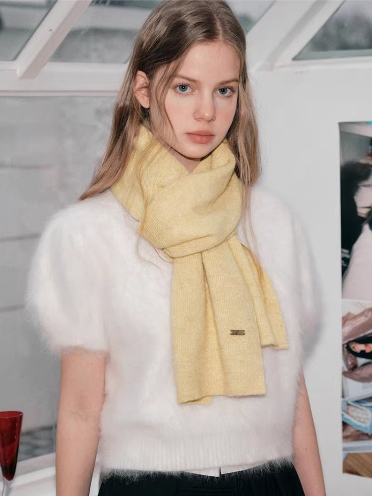 Model wearing a pale yellow knit scarf with a textured pattern and a small gold-tone logo tag.