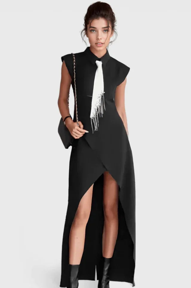 Woman wearing a black sleeveless collared maxi dress with a white tie and silver fringe detail, paired with a black handbag.