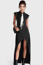 Woman wearing a black sleeveless collared maxi dress with a white tie and silver fringe detail, paired with a black handbag.