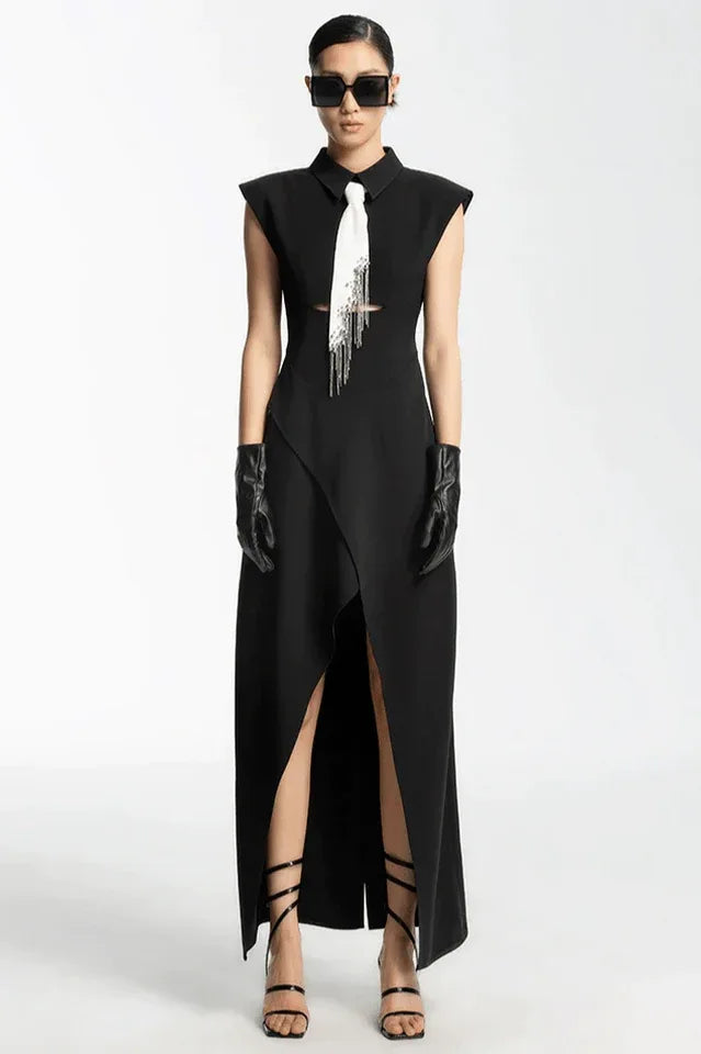 Woman in a black sleeveless collared maxi dress with a white tie and silver fringe detail, black leather gloves, and strappy heels.