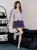 Woman posing in a light purple long-sleeve knit top, purple tiered lace skirt, knee-high socks, and silver shoes