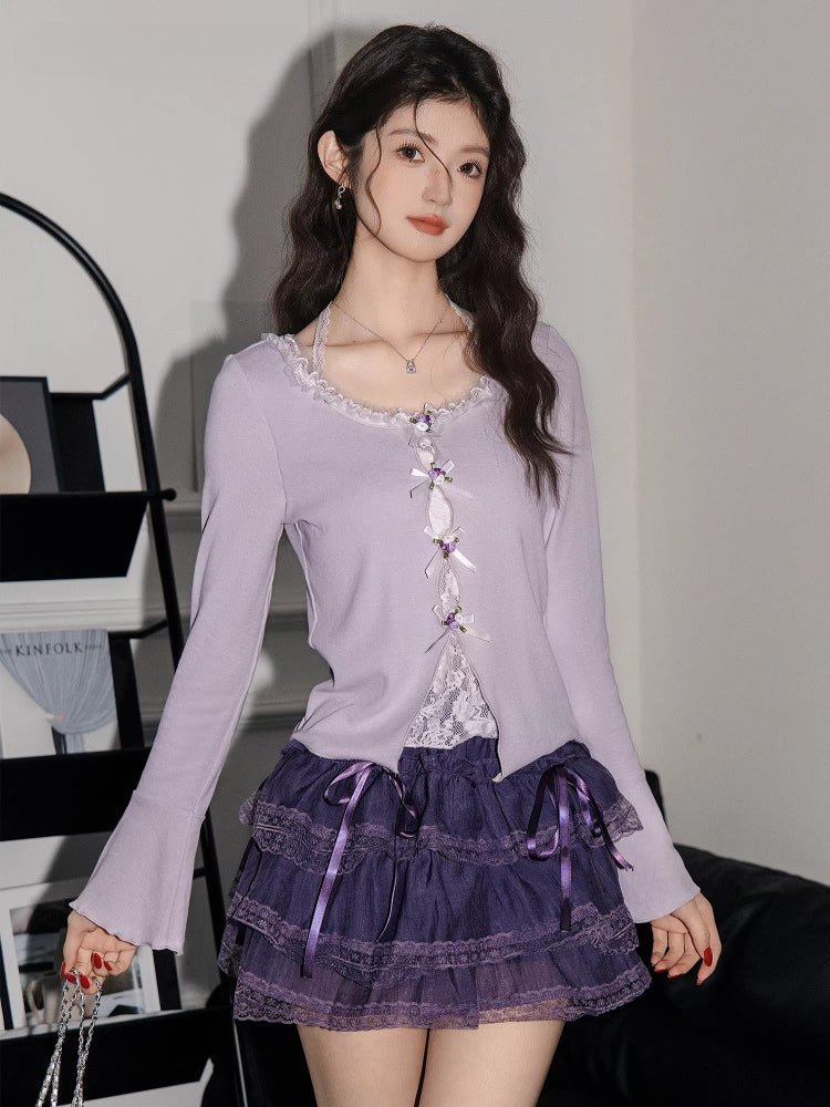 Close-up of a woman's torso wearing a light purple knit top with decorative ties and a purple lace skirt