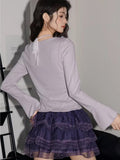Back view of a woman in a light purple long-sleeve knit top and a purple tiered lace skirt