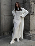 Full body shot of a woman in a white ribbed maxi dress and a white fluffy long cardigan.