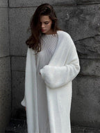 Woman wearing a white fluffy long cardigan over a white ribbed dress.