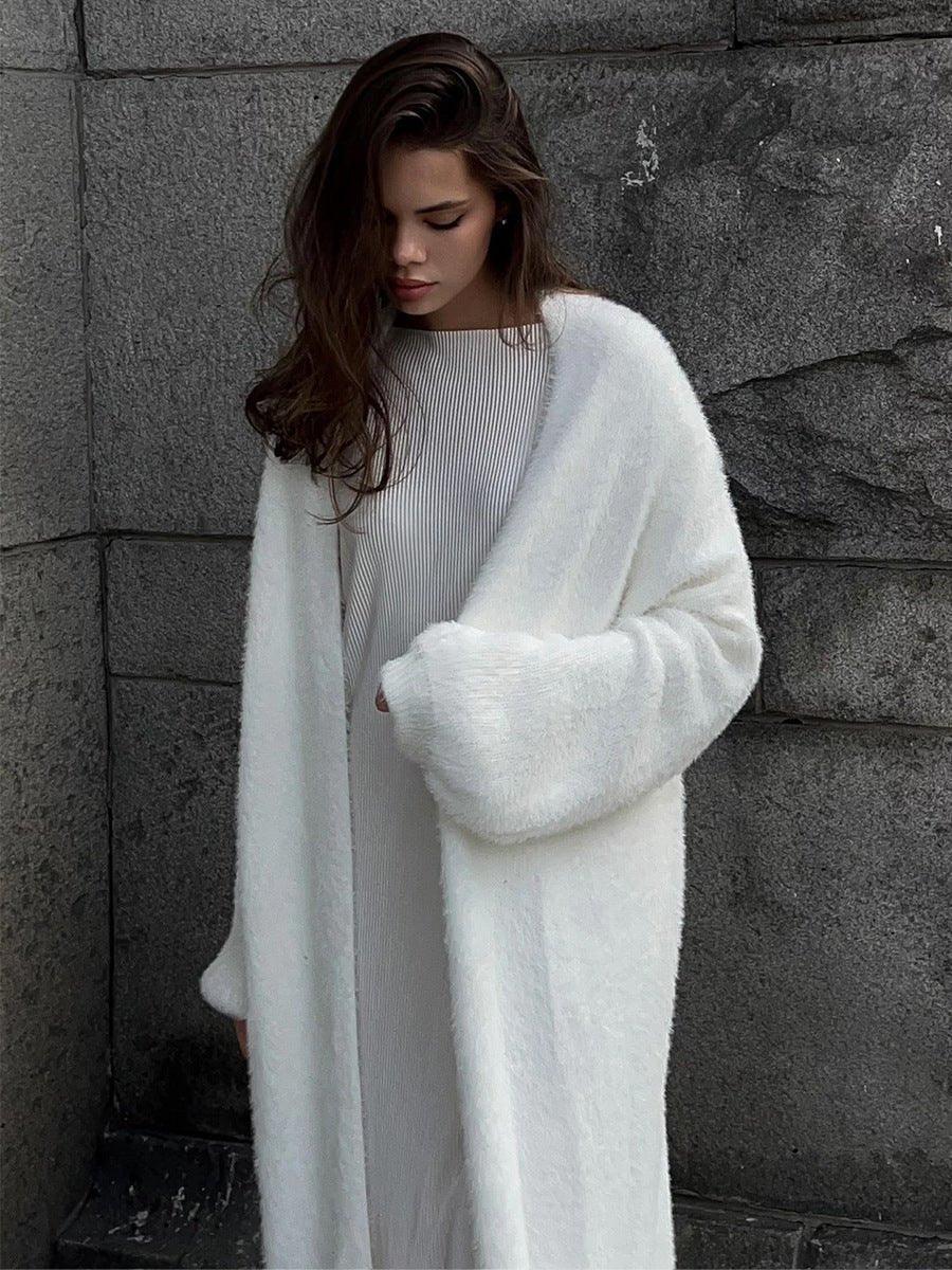 Woman wearing a white fluffy long cardigan over a white ribbed dress.