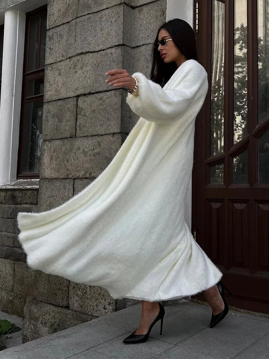 Woman in a white flowing fluffy long cardigan and a white dress, with her arms outstretched.