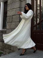 Woman in a white flowing fluffy long cardigan and a white dress, with her arms outstretched.