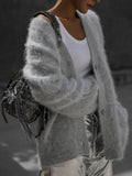 Woman wearing a grey fuzzy knit cardigan over a white tank top.
