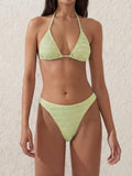 Woman wearing a textured light green bikini set with a halter neck top and high-cut bottoms.