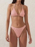 Woman wearing a textured pink bikini set with a halter neck top and high-cut bottoms.