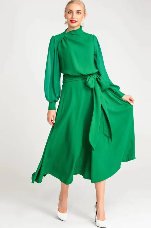 Woman wearing a green long-sleeved A-line dress with a mock neck and self-tie belt, front view