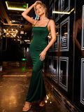 Woman in an emerald green satin mermaid dress with spaghetti straps and a square neckline, posing with one hand on her head.