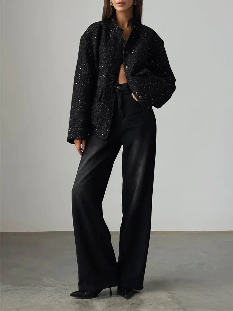 Full body shot of a woman in a black sequined textured cropped jacket and dark wash wide-leg jeans.