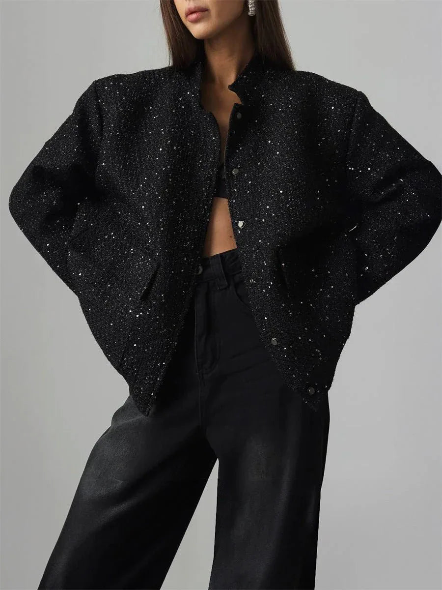 Woman wearing a black sequined textured cropped jacket with wide sleeves and a mandarin collar.