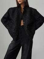 Woman wearing a black sequined textured cropped jacket with wide sleeves and a mandarin collar.