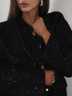Close-up on the chest and neck area of a woman wearing a black sequined textured jacket, showcasing the fabric detail.