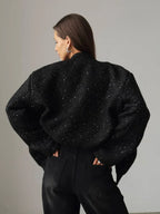 Back view of a woman wearing a black sequined textured cropped jacket, hands in pockets.