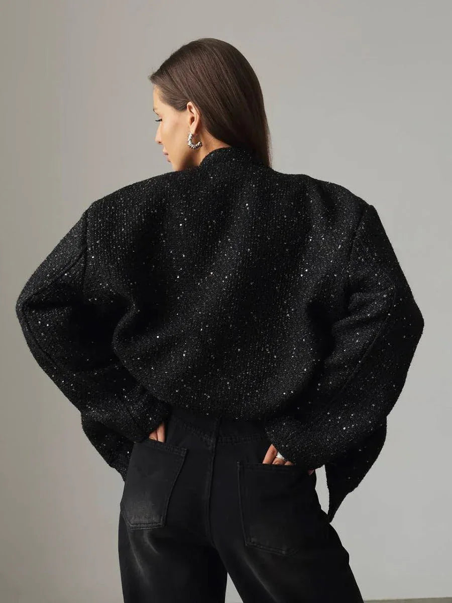Back view of a woman wearing a black sequined textured cropped jacket, hands in pockets.