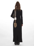 Back view of a woman in a black long-sleeve top and black maxi skirt with a slit detail