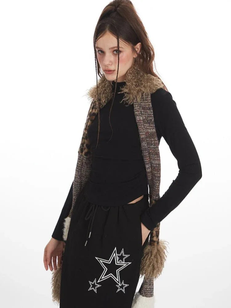 Woman posing in a black long-sleeve top and black maxi skirt with star graphics, wearing a patterned scarf