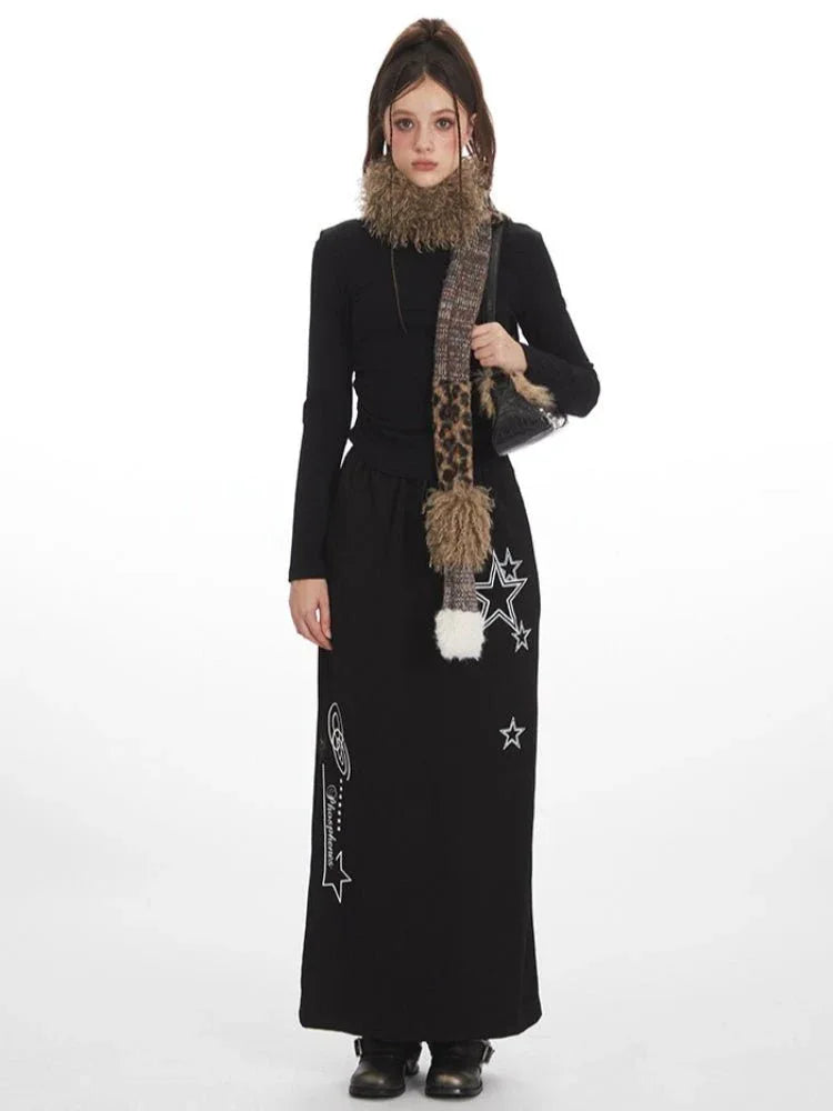 Woman wearing a black long-sleeve top and a black maxi skirt with star graphics, accessorized with a patterned scarf