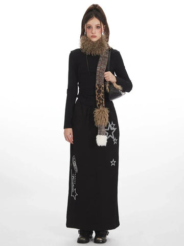 Woman wearing a black long-sleeve top and a black maxi skirt with star graphics, accessorized with a patterned scarf