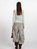 Back view of a woman wearing a light green long-sleeve ribbed knit top with asymmetrical neckline and cold shoulder cutouts.