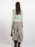 Back view of a woman wearing a light green long-sleeve ribbed knit top with asymmetrical neckline and cold shoulder cutouts.