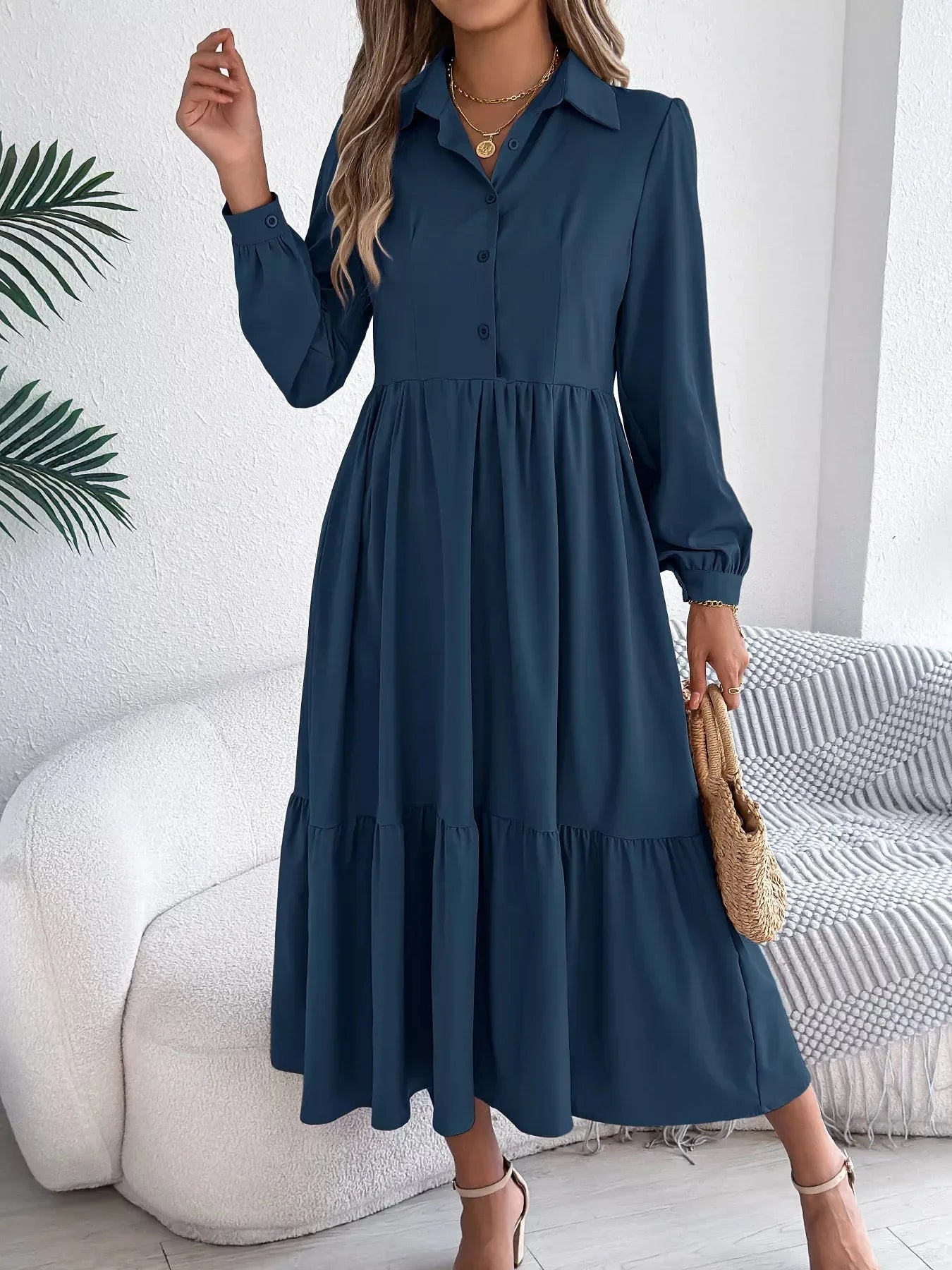 Woman standing and showcasing a navy blue collared midi dress with long sleeves and a tiered hem.