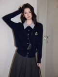 Woman wearing a navy blue cable knit cardigan with a striped collar and embroidered emblem