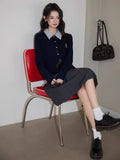 Full body shot of a woman in a navy blue cable knit cardigan and pleated skirt