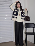 Full body shot of a woman in a navy and cream knit zip-up vest, black jeans, and cream turtleneck