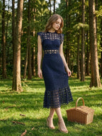 Woman in a navy blue lace midi dress with a high neckline and ruffled cap sleeves, standing in a forest with a picnic basket.